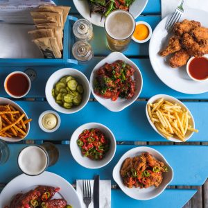 an overhead shot of crunchy fresh salad, fried chicken and sides, on a bright blue table